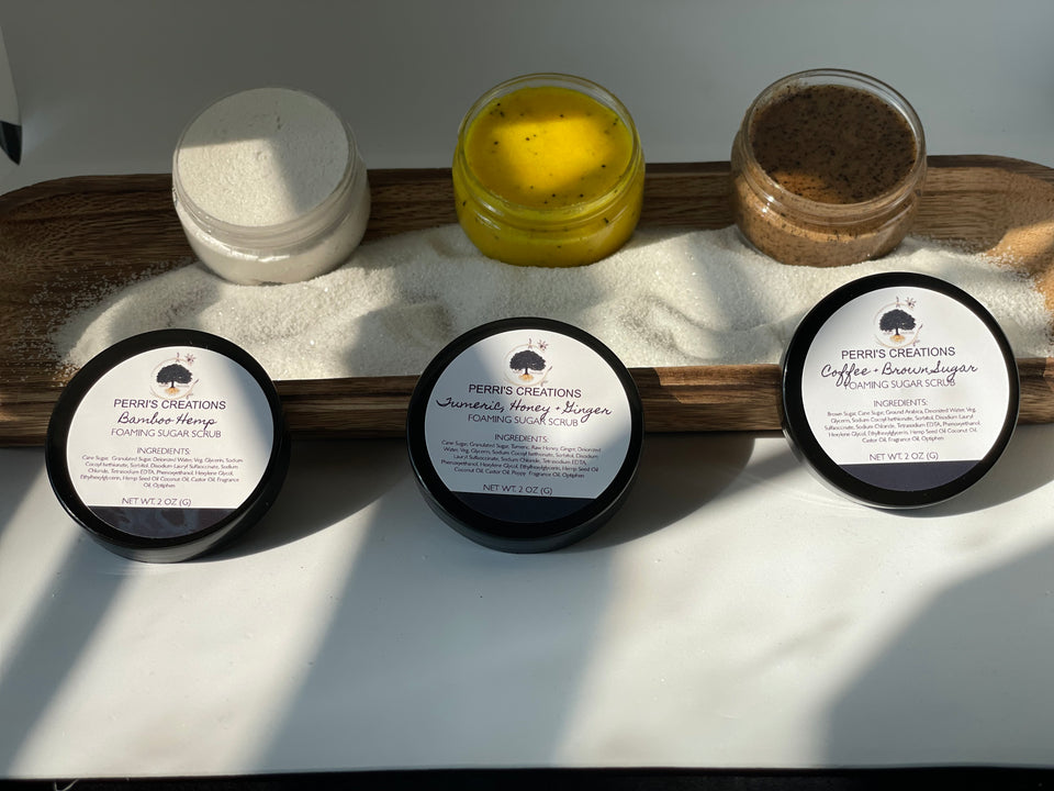 foaming sugar scrubs, bamboo hemp, tumeric honey ginger, coffee and brown sugar on wooden tray with sand